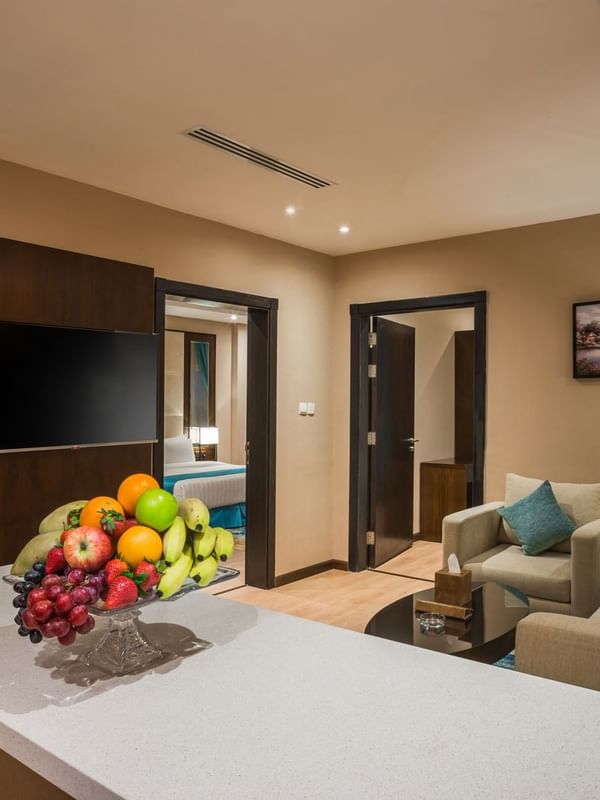 Fruit bowl on a counter by plush sofas and a TV under recessed lights in Family suite at Naviti By Warwick Dammam