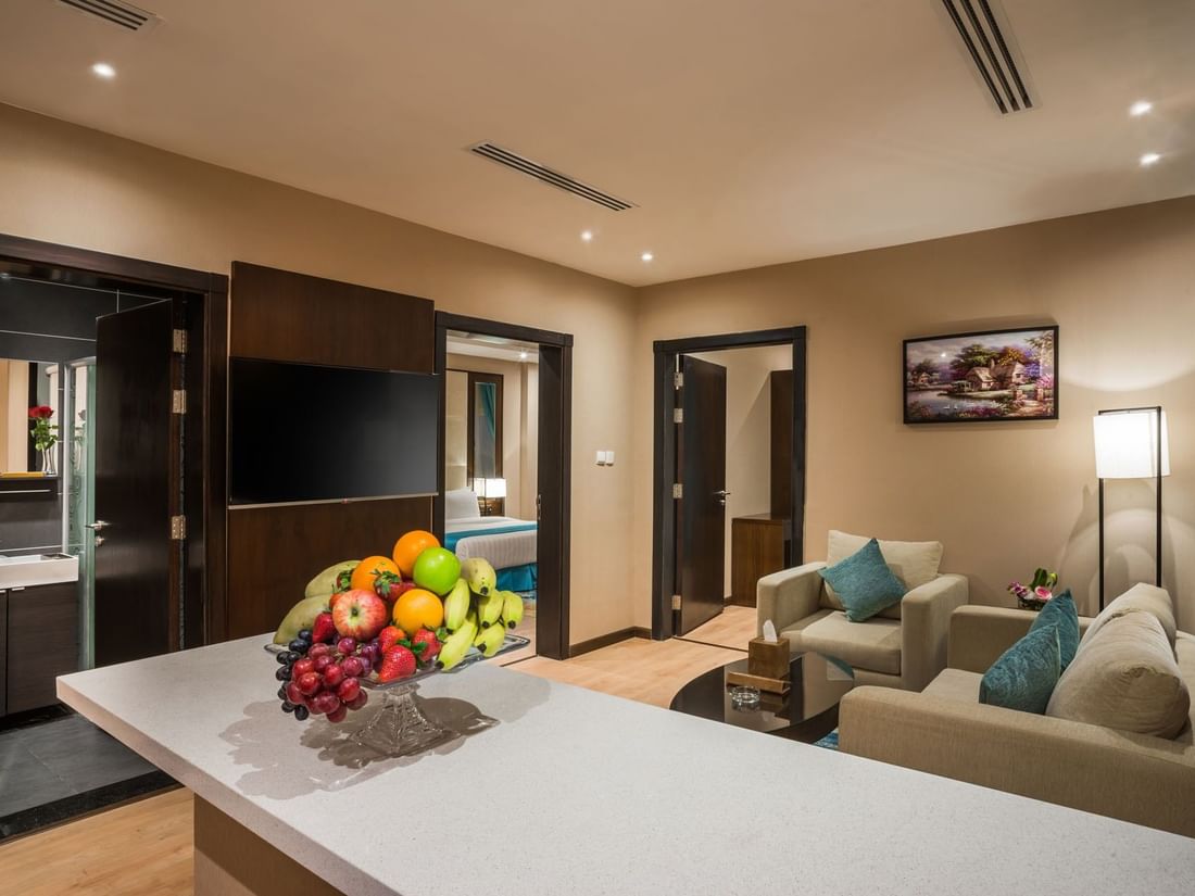 Fruit bowl on a counter by plush sofas and a TV under recessed lights in Family suite at Naviti By Warwick Dammam
