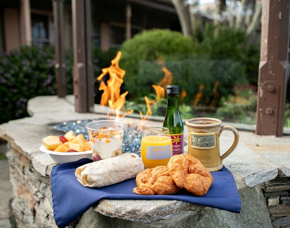 Breakfast wrap and croissants by a mug under a warm flame, surrounded by a blue napkin on a stone at Sea Otter Inn