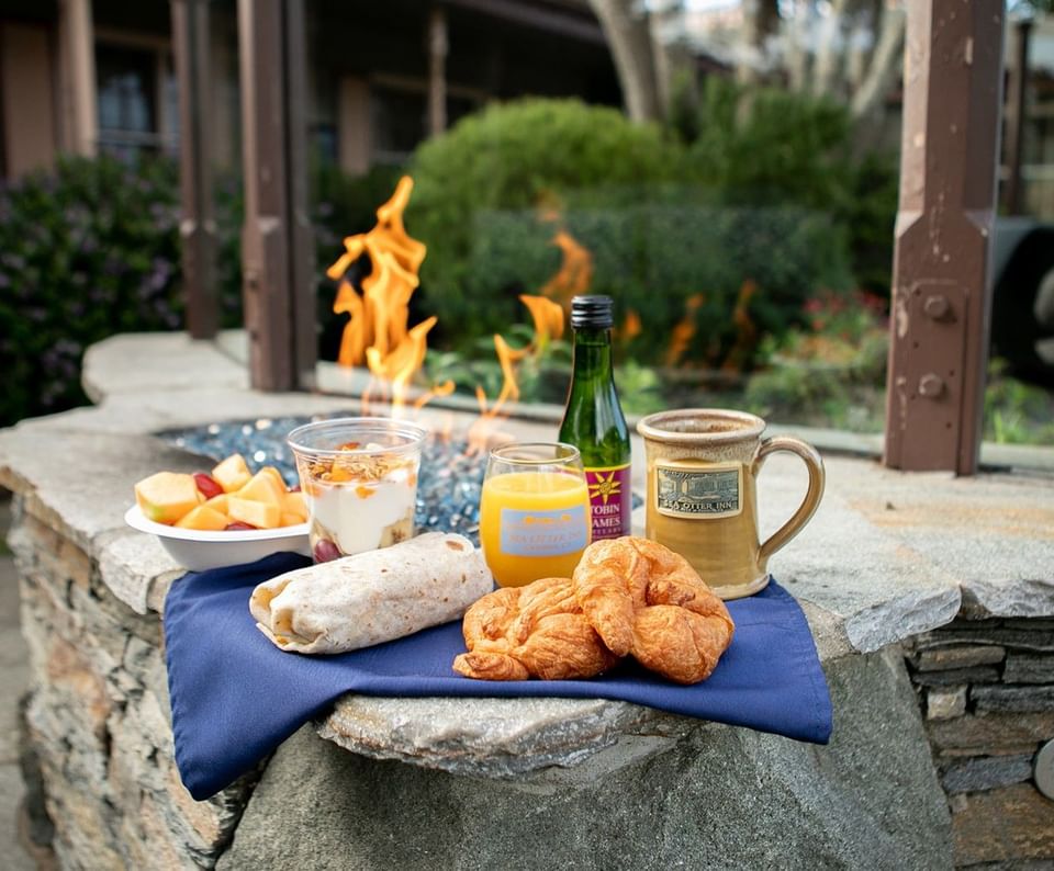 Breakfast wrap and croissants by a mug under a warm flame, surrounded by a blue napkin on a stone at Sea Otter Inn