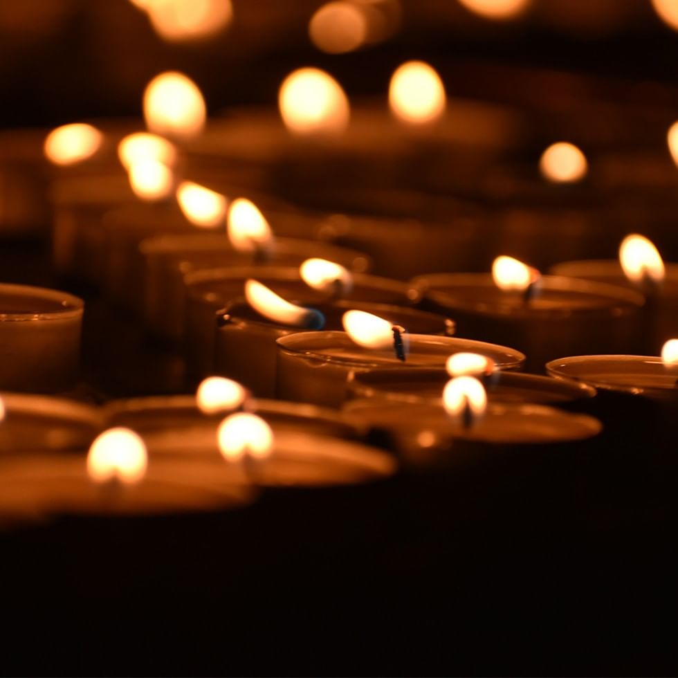 Molte candele accese con fiamme luminose, disposte in file, in un ambiente buio.