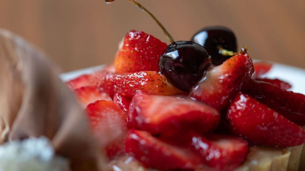 Close-up of a dessert tart topped with glossy sliced strawberries and cherries in Artist Lobby Lounge at Warwick Hotel Jeddah