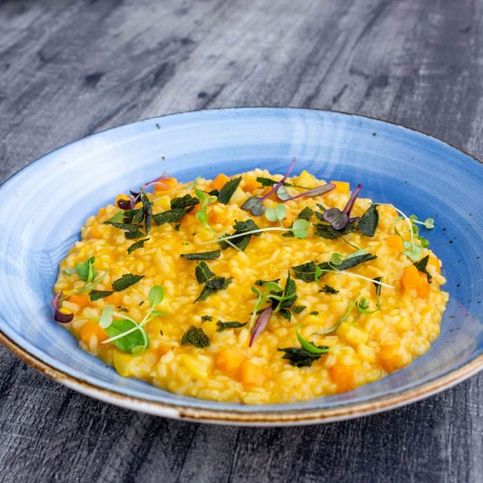 Blue bowl filled with creamy risotto garnished with green herbs on a wooden table.