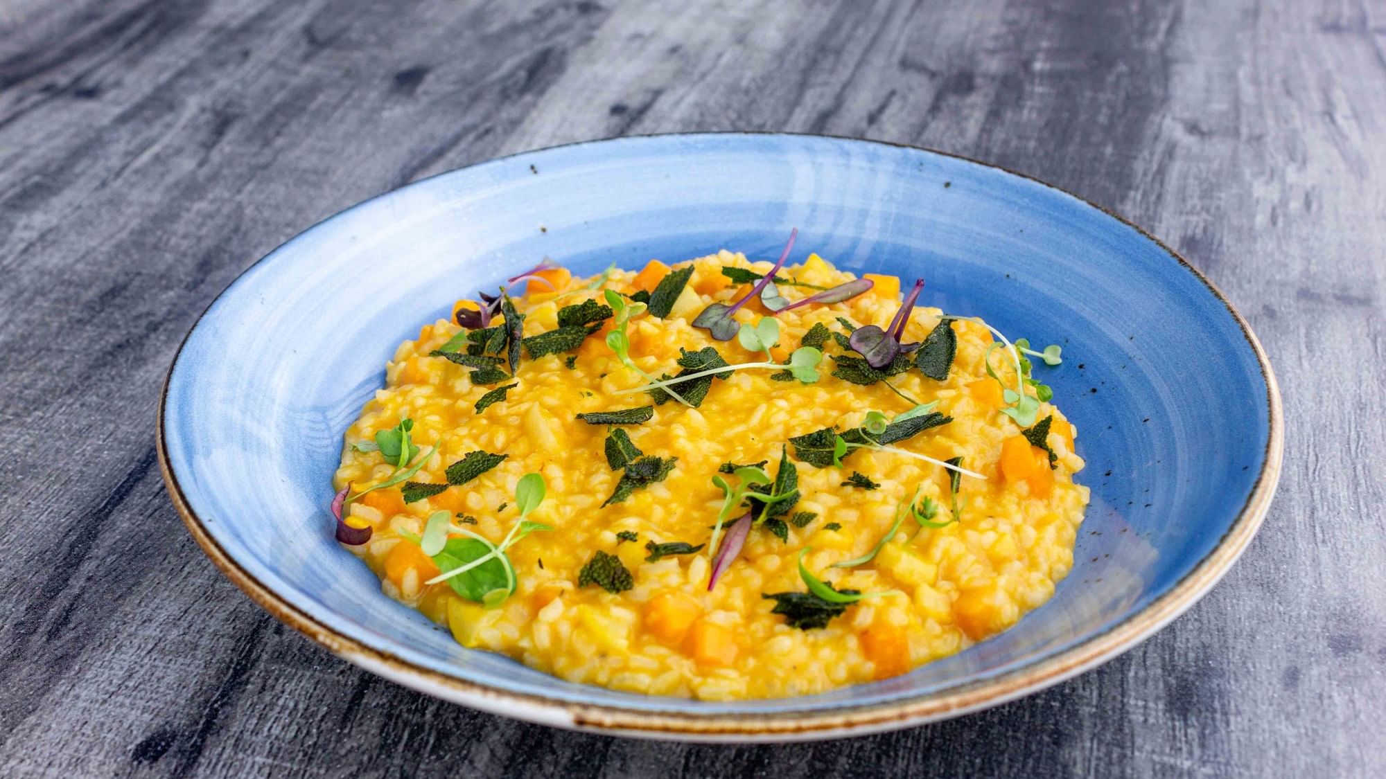 Blue bowl filled with creamy risotto garnished with green herbs on a wooden table.