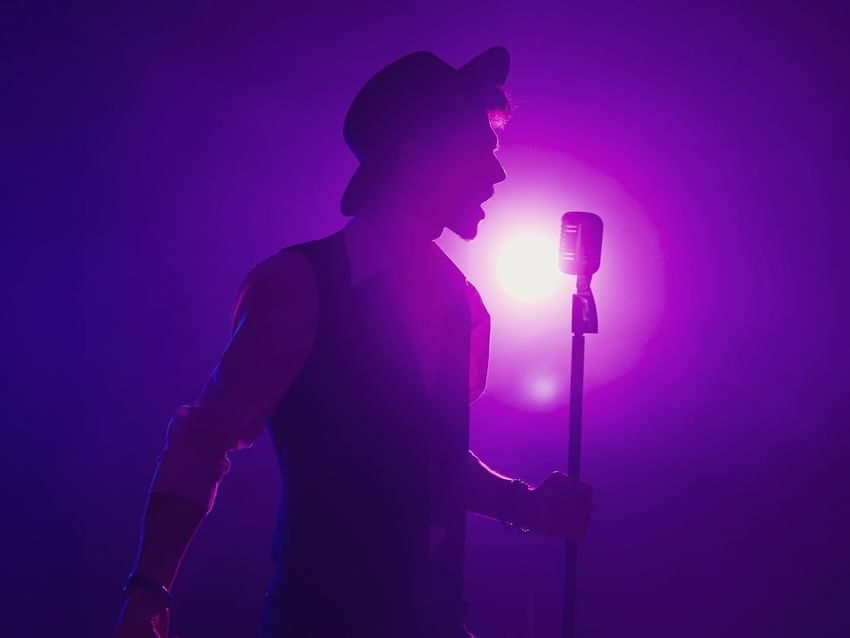 Silhouette of a male singer in a hat performing into a vintage microphone under purple lights at Camino Real