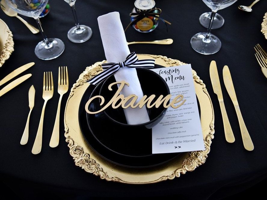 Close-up of an elegant black and gold table setting with a personalized place card, menu, and cutlery at The Sebel Brisbane
