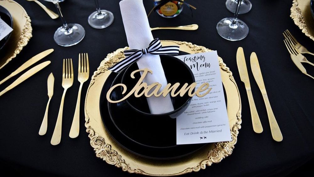 Close-up of an elegant black and gold table setting with a personalized place card, menu, and cutlery at The Sebel Brisbane
