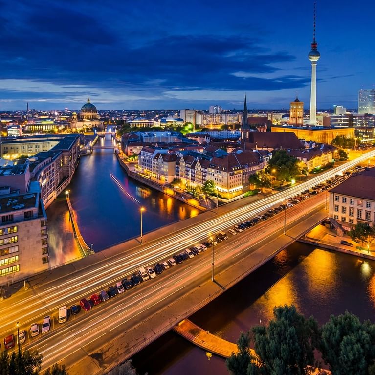 Aerial view of Berlin's illuminated skyline at dusk featuring the TV Tower and Spree River with light trails from traffic.