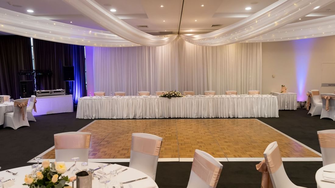 Wedding reception hall with a decorated bridal table, dance floor, and draped ceiling lights at Mercure Kooindah Waters
