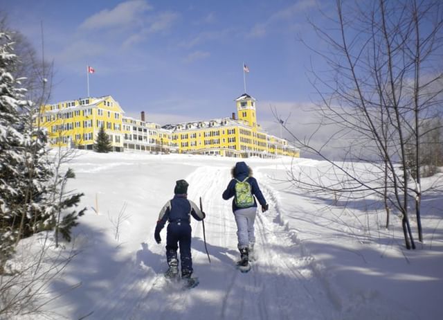 Two visitors snowshoeing on a wintry trail facing Mountain View Grand Resort & Spa on a winter hill surrounded by snowed