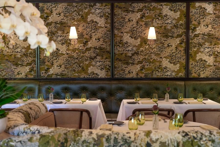 Cafe Boulud dining room with green leather banquettes, and tables set with white tablecloths and green glasses.
