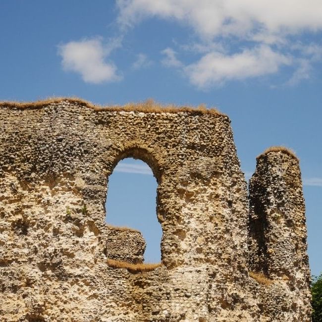 Ancient stone ruins of Reading Abbey with an arched window opening against a blue sky with white clouds.