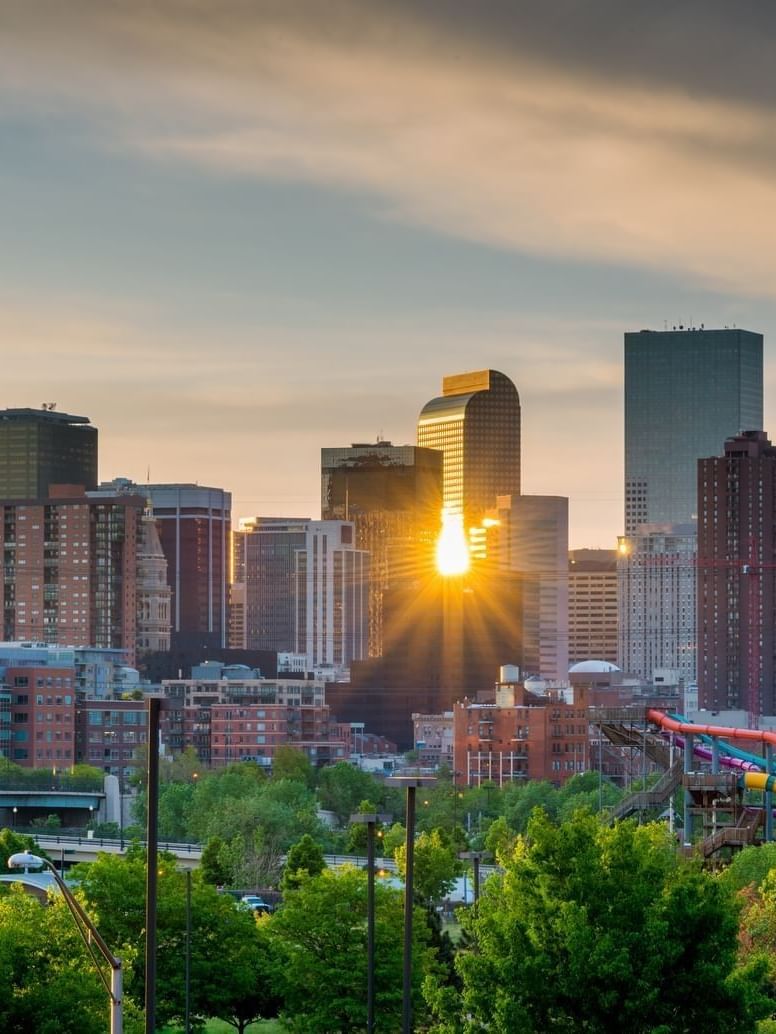 City skyline by green trees under a sunset sky near skyscrapers near Warwick Denver