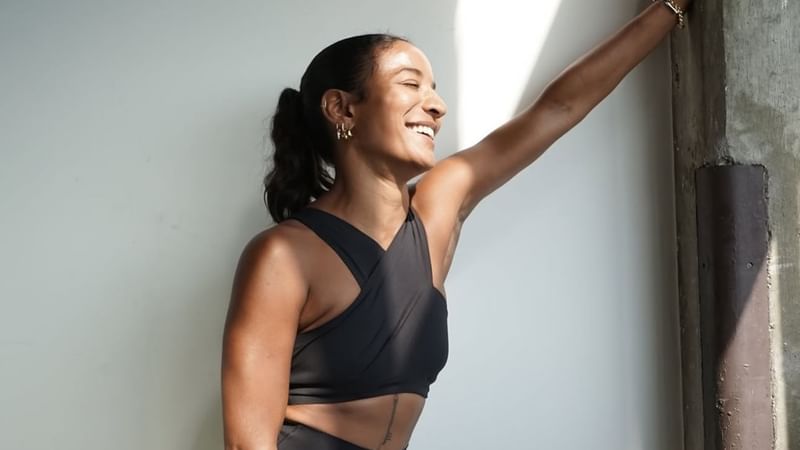Smiling woman in black athletic wear, leaning against a wall at The Londoner Hotel