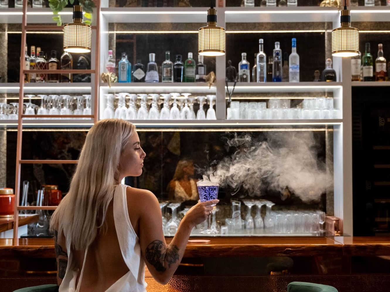 Elegant blonde woman holding a smoking cocktail at a vibrant bar at Paramount Hotel Midtown