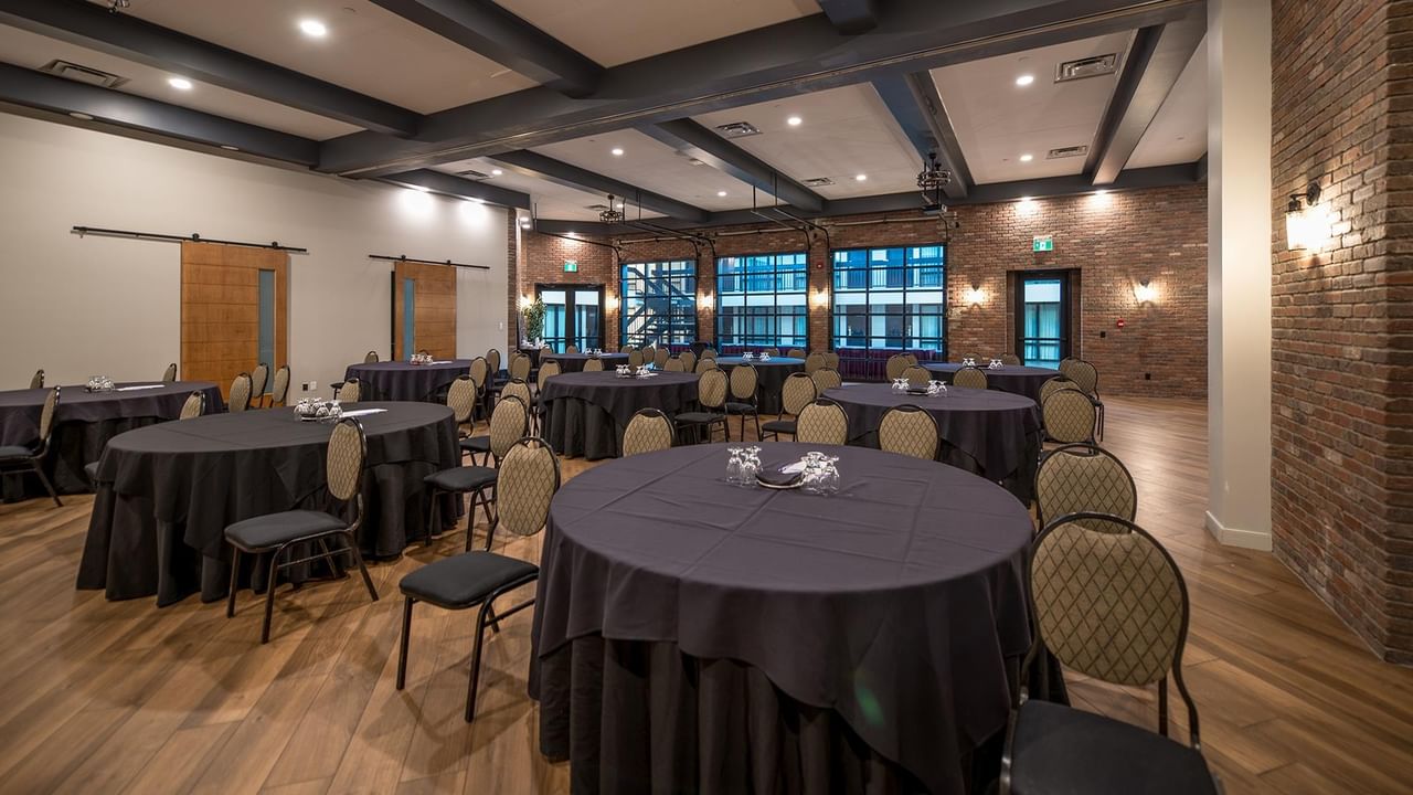 Elegantly set round tables with black tablecloths and chairs in a spacious event room.