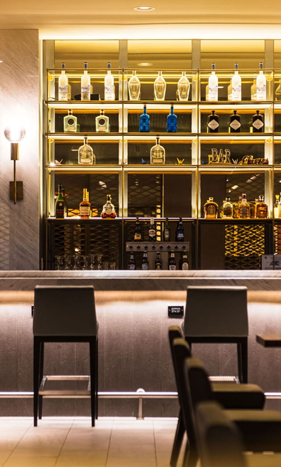 Well-lit shelves of liquor bottles and bar counter in Bogart's Lounge at APA Hotel Woodbridge