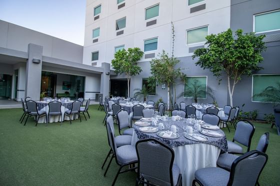 Outdoor event with round tables by grey chairs at Hotel Mirra, hotel with meeting rooms in San Luis, Sonora for events