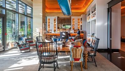 Cozy lounge by floor-to-ceiling windows, with a wooden bar backdrop at The Residences at Seafire