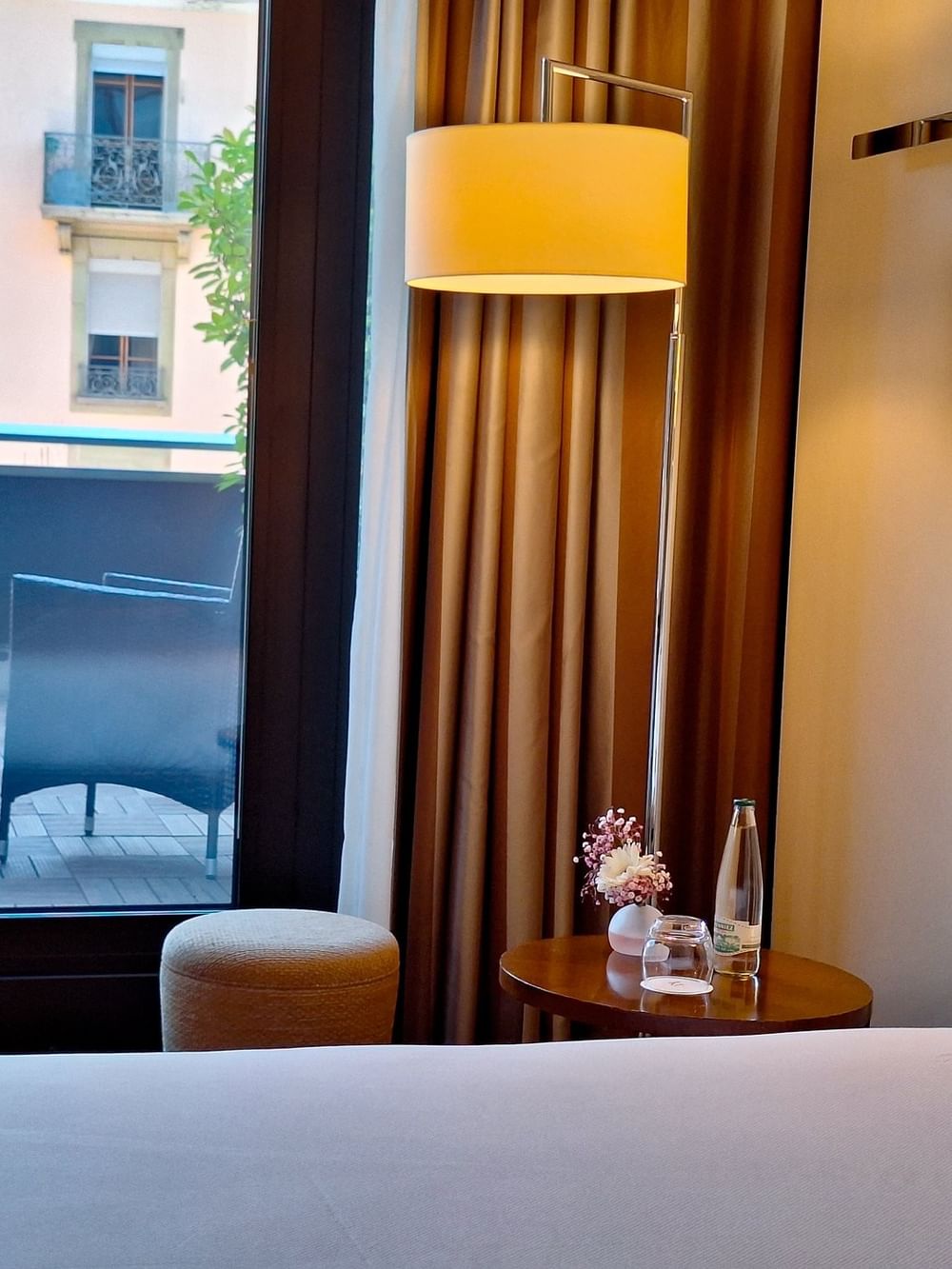 Round table by a bed under a floor lamp with chairs on a balcony in Deluxe Terrace Room at Warwick Geneva