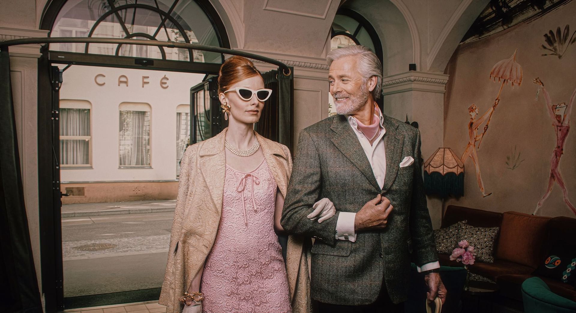 Well-dressed couple stands at the café entrance, with colorful decor and a city street view at Hotel Motto Vienna