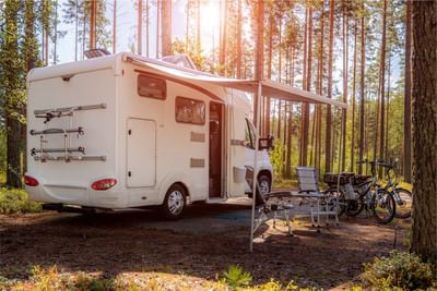 White motorhome is parked in a sunny forest, with an awning extended, a table and chairs at Fall Creek Marina & Campground