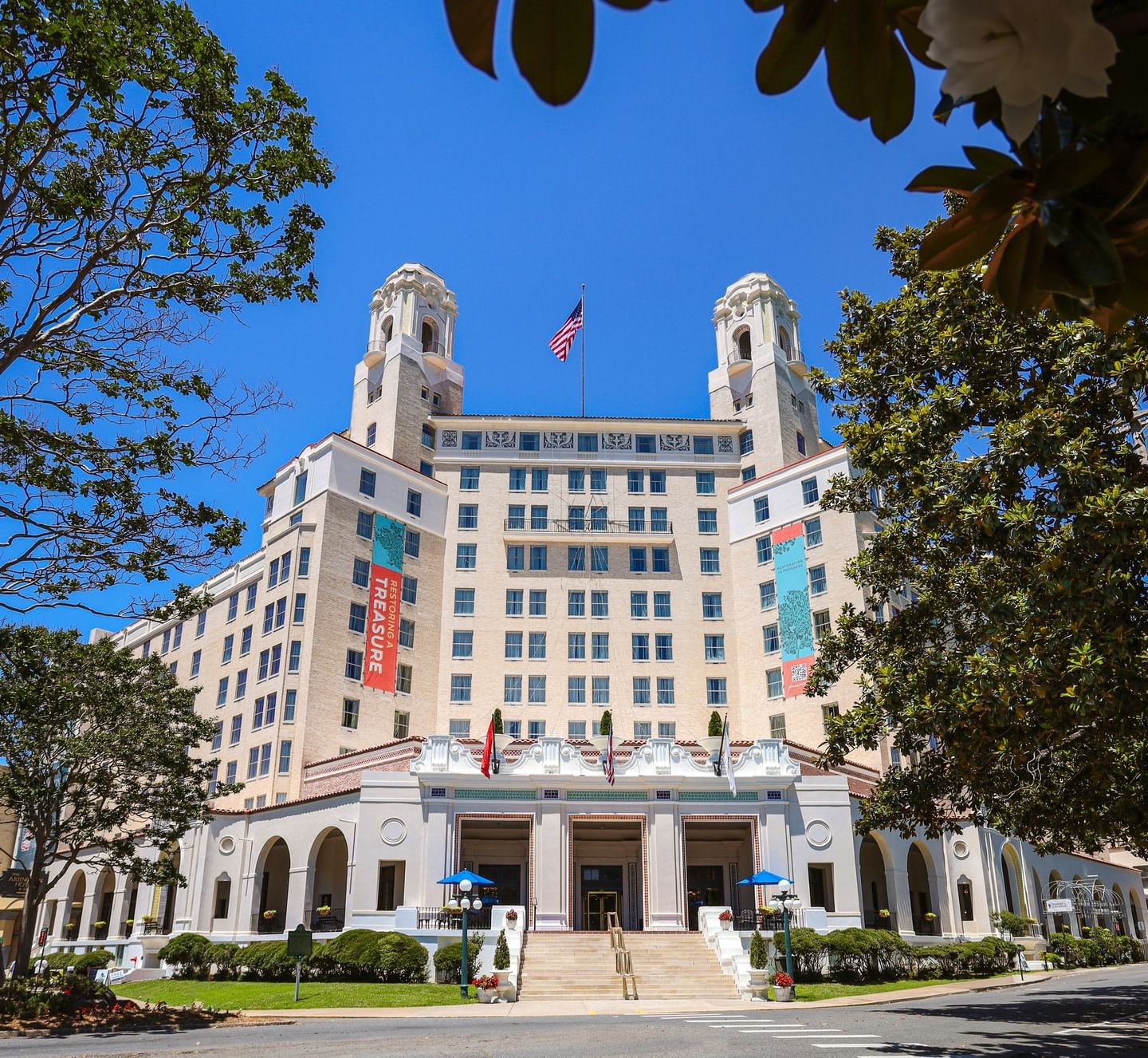 Manicured hedges by stone stairs under a bright blue sky surrounding the iconic Arlington Resort Hotel & Spa