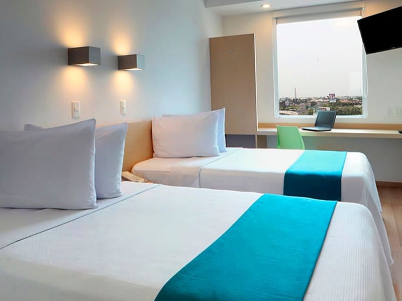 Modern room at Fiesta Americana Travelty with two white beds, soft-glowing wall lamps, and a window-side desk