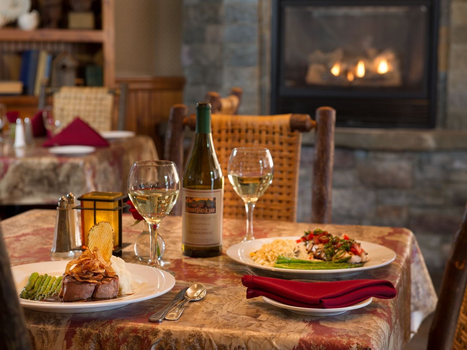 Steak and wine by a lit candle under a fireplace glow at the Cambria Pines Lodge Restaurant in Sea Otter Inn