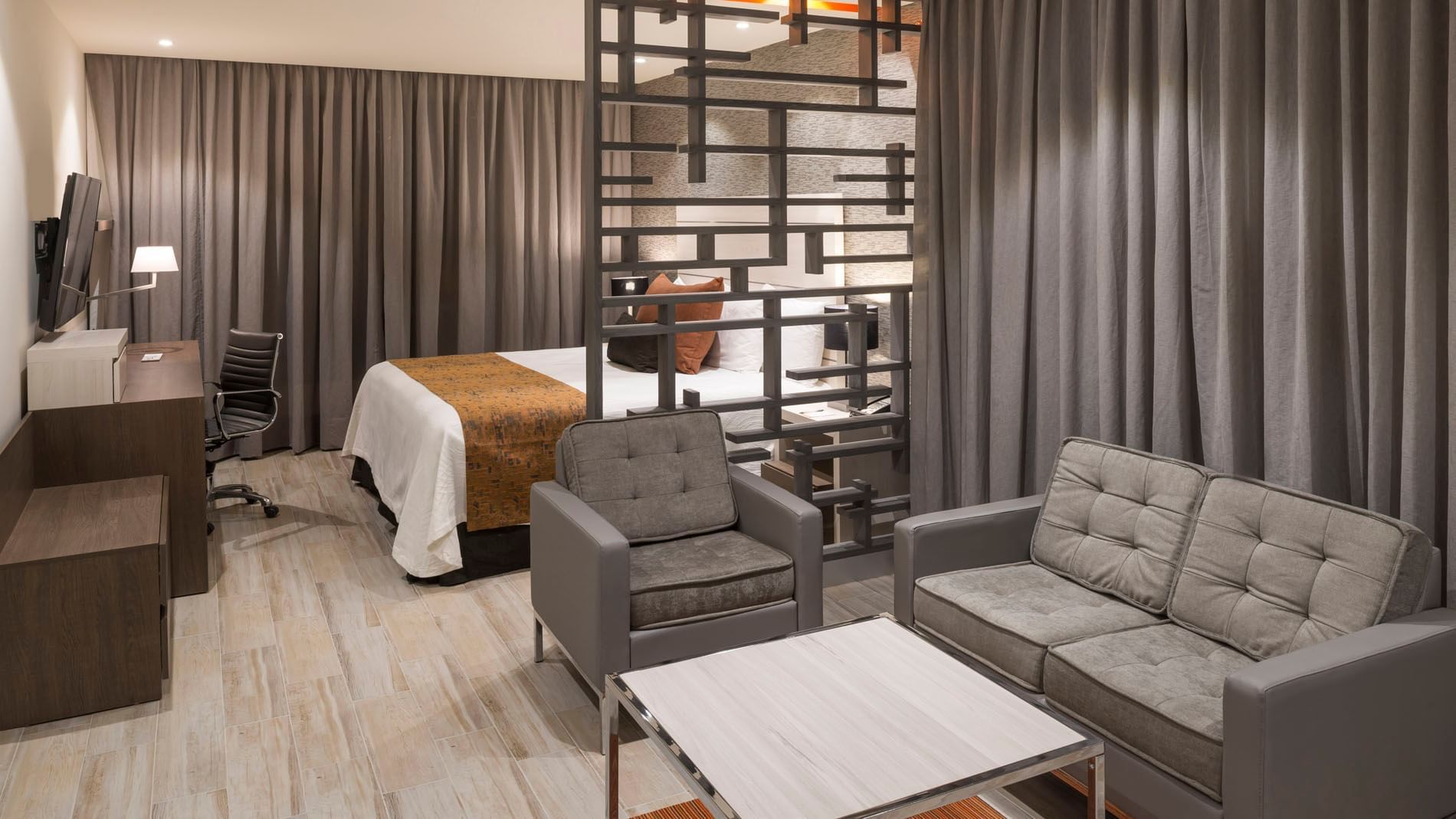 King Long Stay Suite seating area at Real Inn Celaya with a modern grey sofa, coffee table, and a decorative room partition