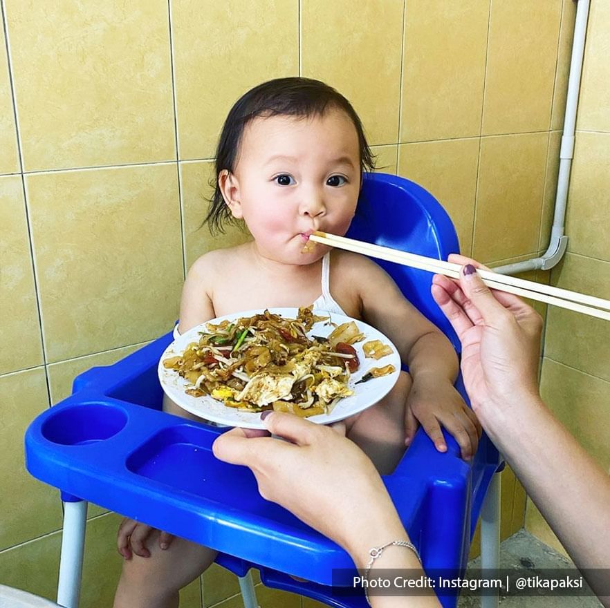 a toddler was eating the famous Siam Road Charcoal Char Kway Teow while sitting on a high chair