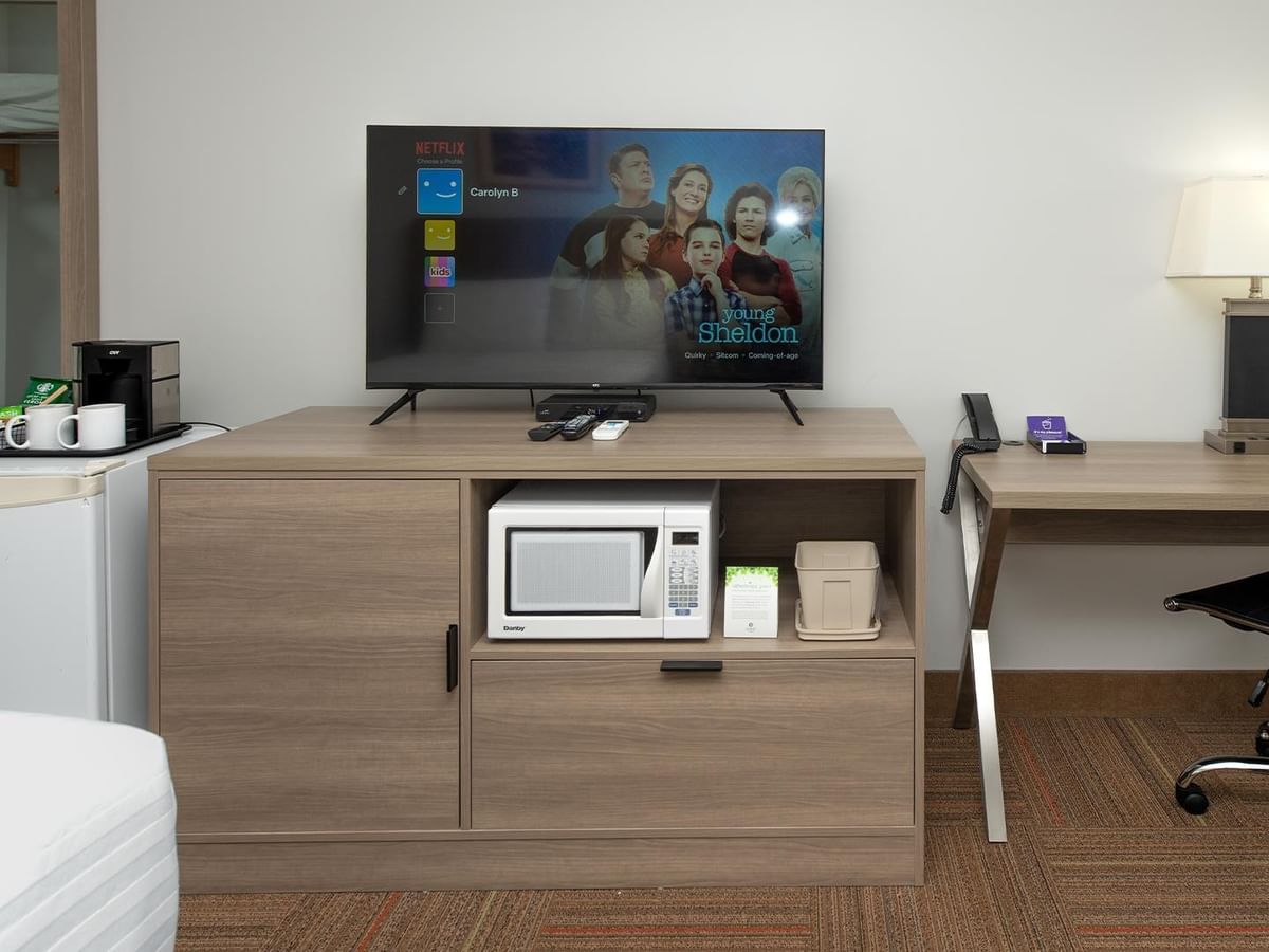 Coast Queen room with wooden desk, flat-screen TV, microwave, mini-fridge, and work area.