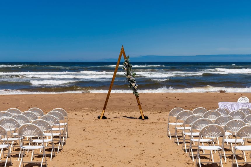 Triangle wedding arch and rows of white chairs on the beach for a Pei Beach wedding at Rodd Crowbush Golf & Beach Resort