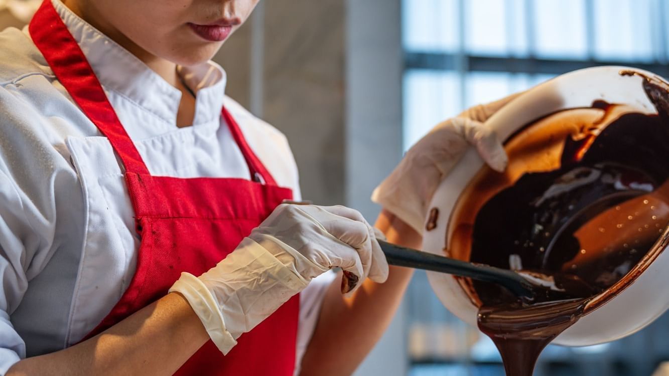 Chef at Paramount Hotel Dubai pouring decadent chocolate from a bowl, preparing a gourmet dessert