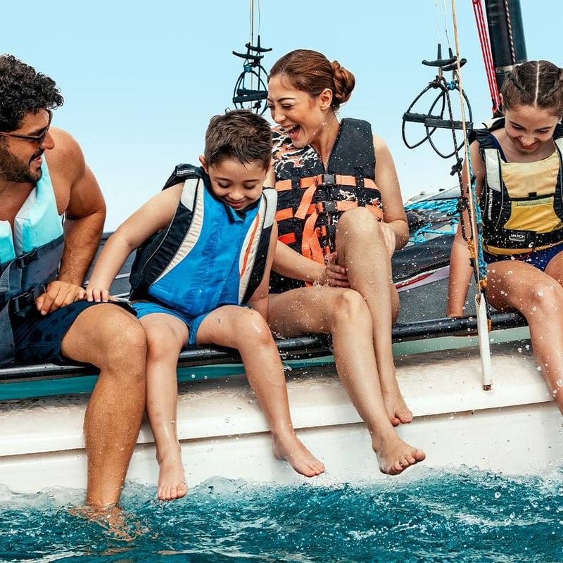 Famiglia in barca, genitori con figli indossano giubbotti di salvataggio, sorridono e godono dell'acqua.