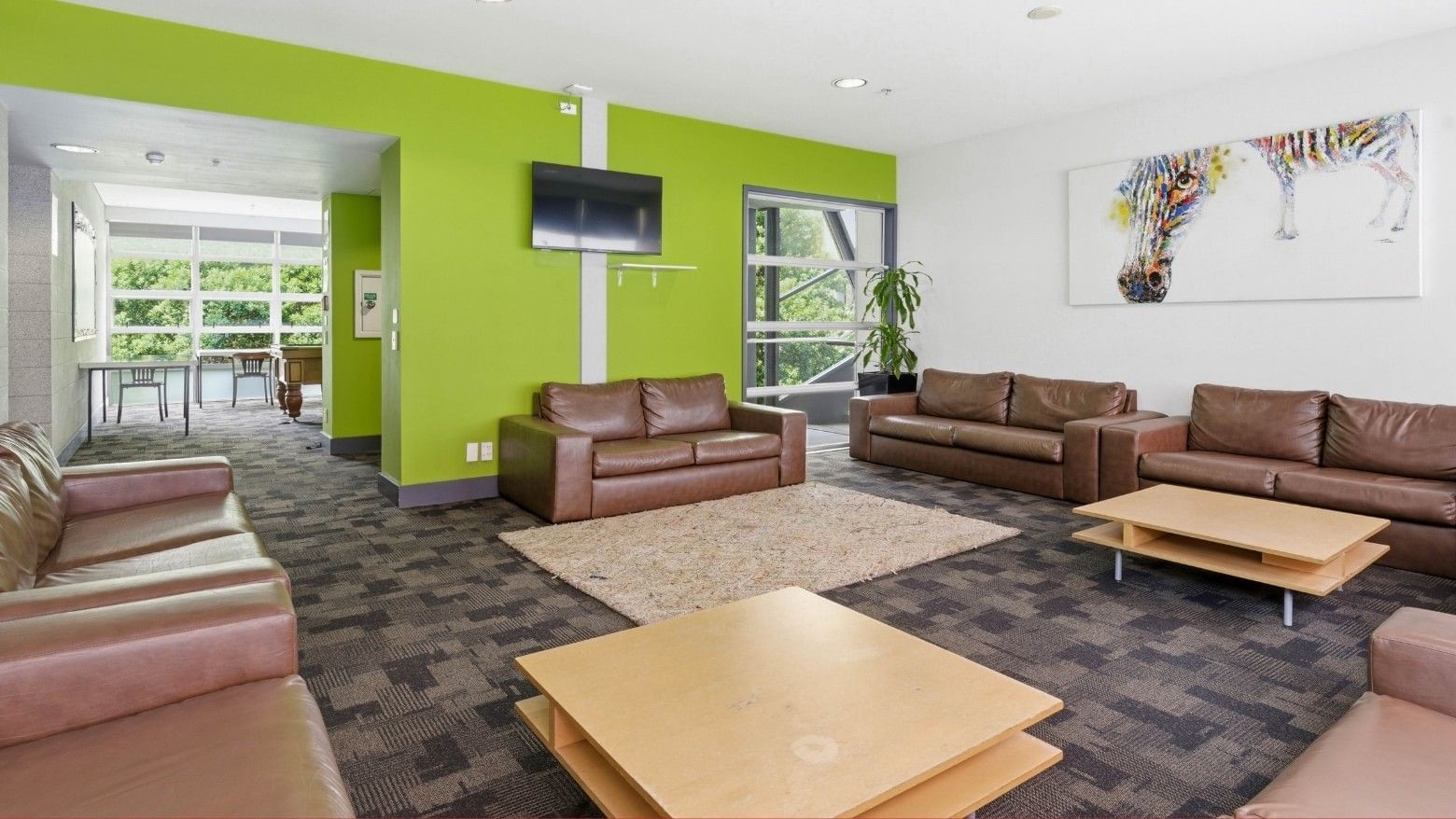 Brown couches and wooden tables in a green and white lobby at Student Living Auckland Anzac.