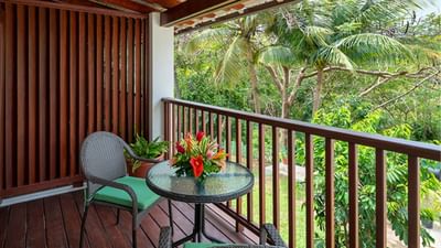 Glass table with flowers and two chairs on a wooden balcony overlooking lush trees in Garden View Room at Sugar Cane Club