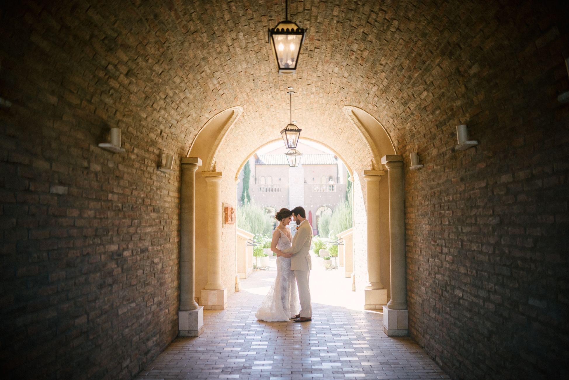 Bride and groom stand face to face under a stone archway