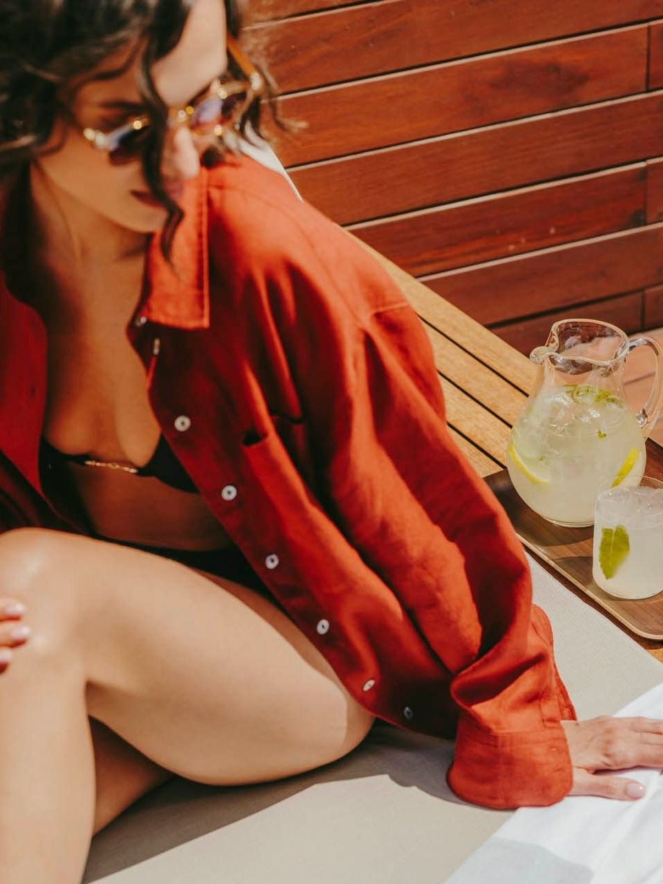 Woman in red shirt relaxing on lounge chair with lemonade and towel, representing Voluptate velit.