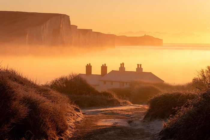 Sunset over the sea with a white house and path leading to the shore.