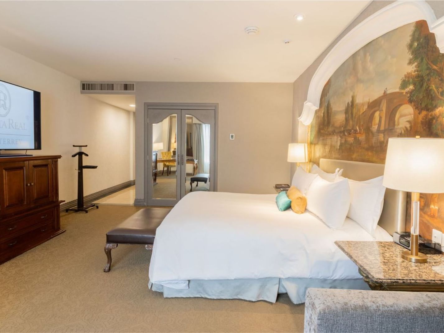 King Executive Tower detailed mural wall behind a large bed with a marble nightstand and gold lamps at Quinta Real Monterrey