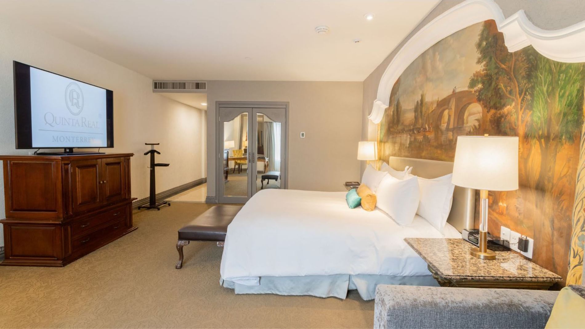 King Executive Tower detailed mural wall behind a large bed with a marble nightstand and gold lamps at Quinta Real Monterrey