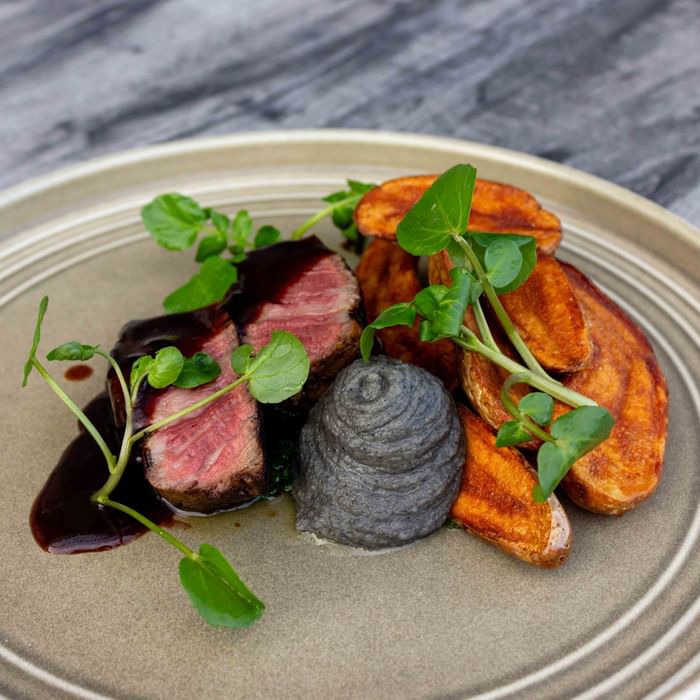 Plate with steak, mashed potatoes, brown sauce, and green garnish on a gray surface.