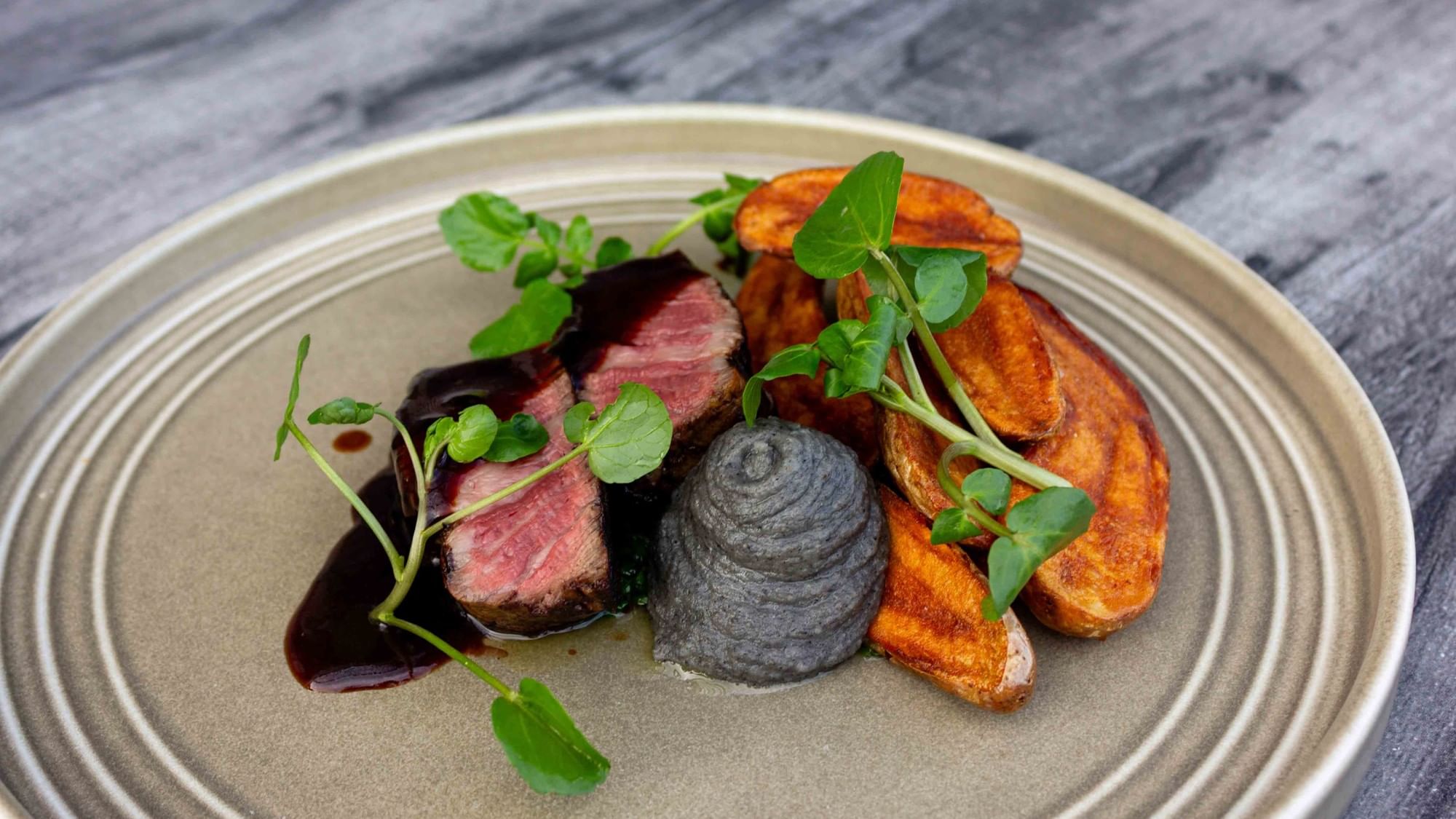 Plate with steak, mashed potatoes, brown sauce, and green garnish on a gray surface.