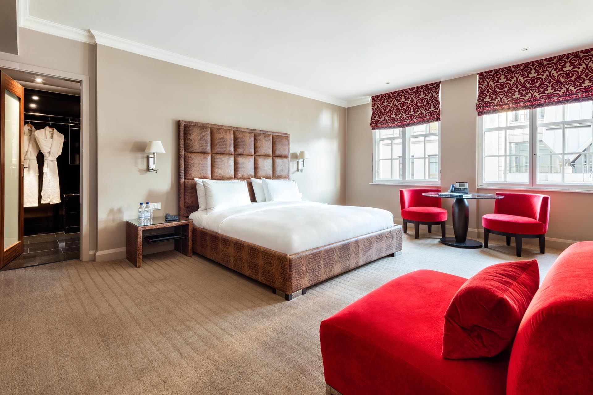 Interior of Collection Premium Room with a large bed, vibrant red seating, and a walk-in wardrobe at The May Fair Hotel