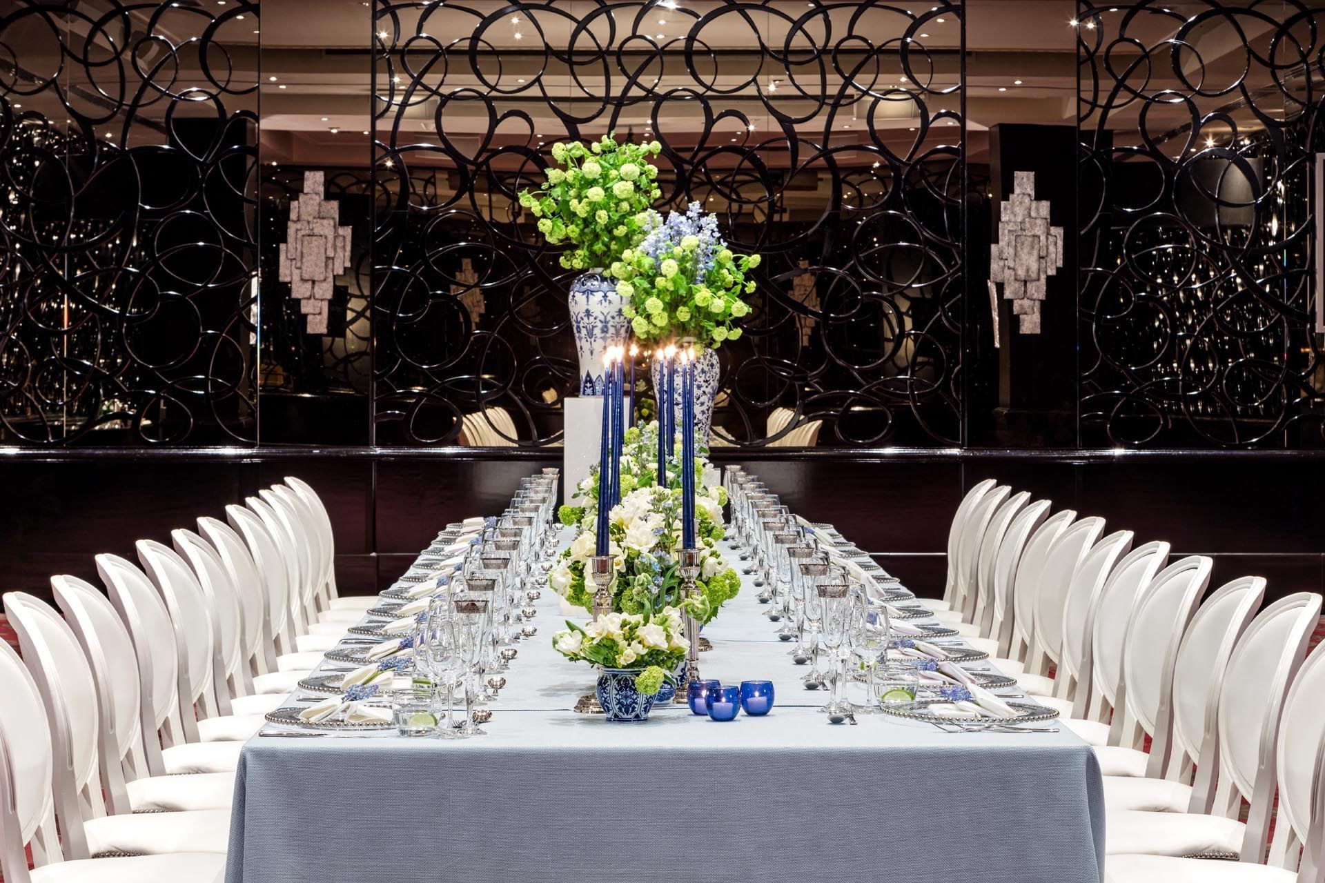Elegantly set long dining table with blue and white floral arrangements and candles at The May Fair Hotel