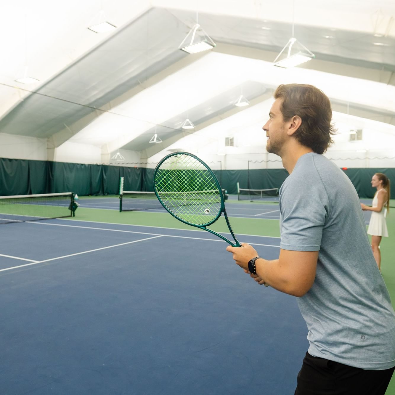 Man with tennis racket looking towards net during a 3.0+ Tennis Doubles Clinic.