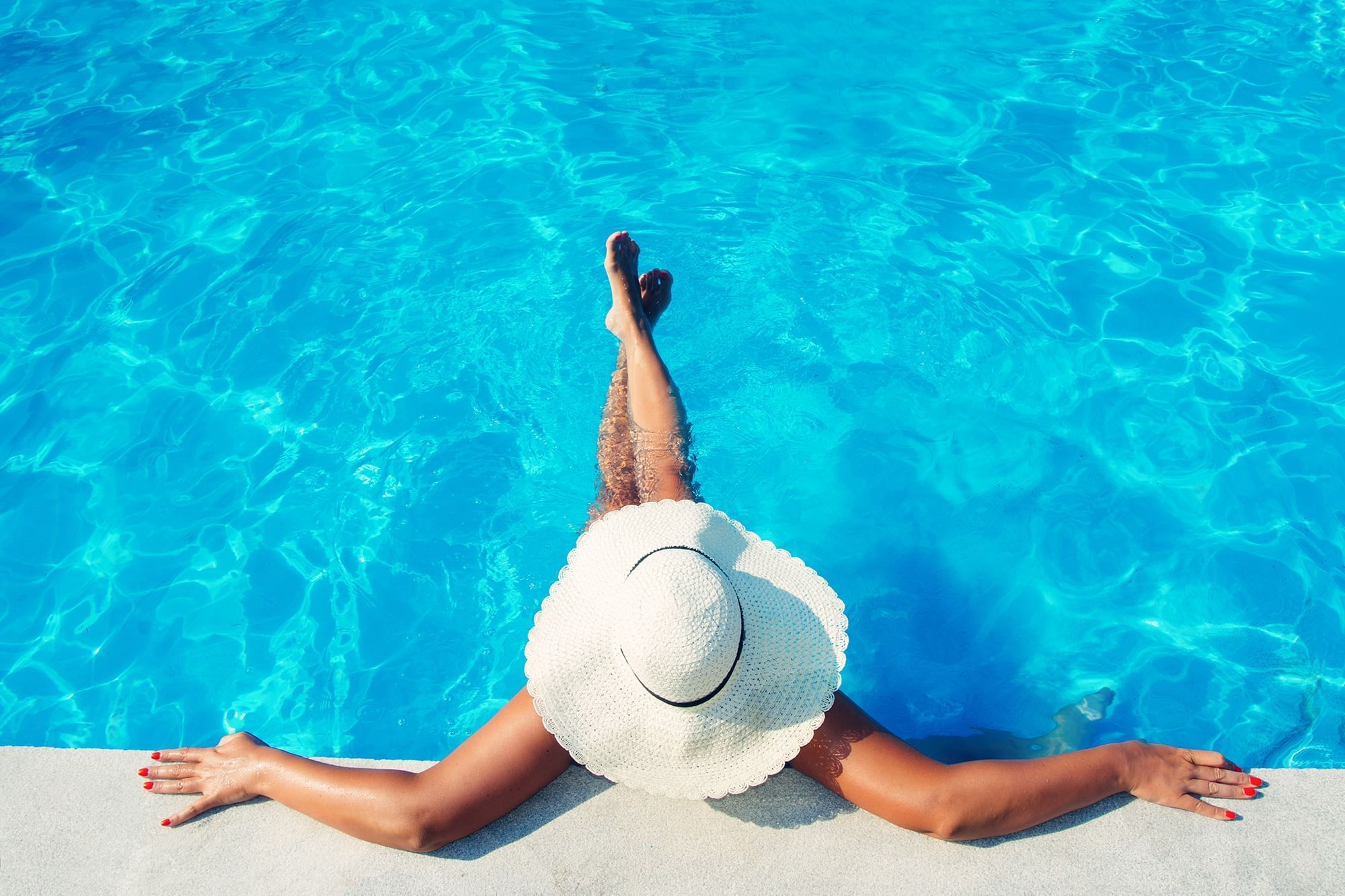 Woman in hat relaxing by the pool at Warwick Melrose Dallas