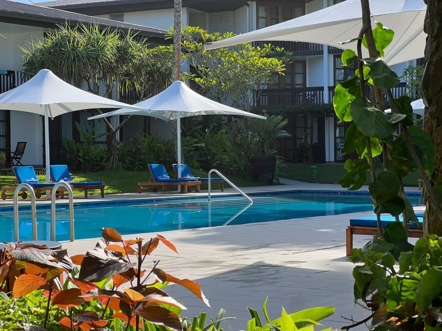 Swimming pool with blue lounge chairs under umbrellas at Warwick Fiji Resort and Spa.