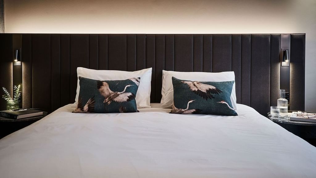 Superior Suite with king bed, dark paneled headboard, bird-print pillows, and bedside lamps at Pullman East Melbourne